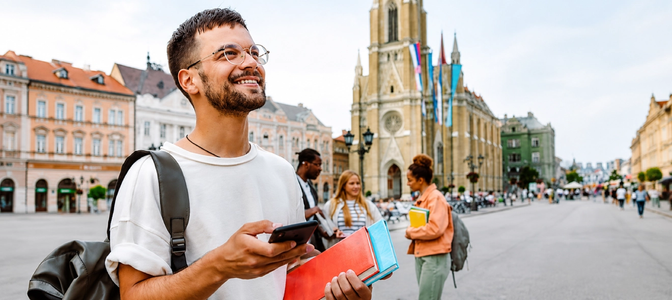 A study abroad student holds books and a smartphone while exploring a city