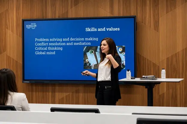 Miriam Jiménez, Associate Dean of International Relations and Diplomacy at Schiller International University, stands in front of a digital whiteboard in a classroom